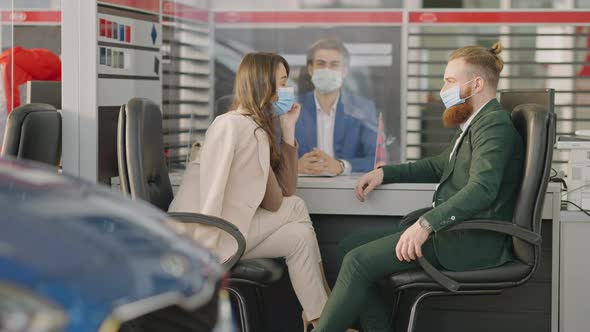Wealthy Caucasian Young Couple in Covid Face Masks Sitting in Car Dealership with Employee Behind alt