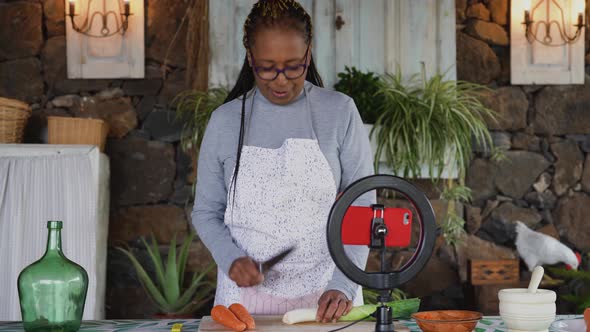 African senior woman preparing food recipe while streaming online with mobile smartphone alt