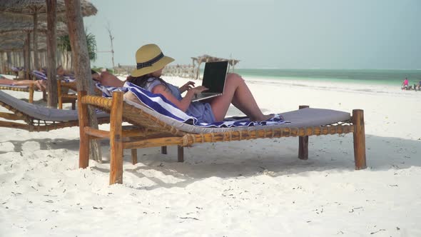 Young Woman Uses Laptop On White Beach Near Ocean alt