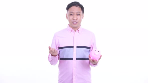 Happy Japanese Businessman Talking While Holding Piggy Bank alt