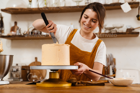 Beautiful happy pastry chef woman smiling while making cake with cream ...