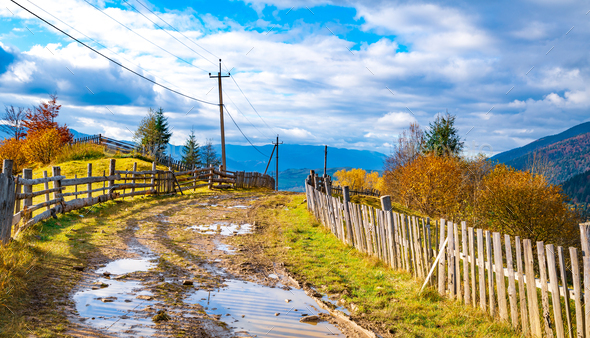 A path along the ridge of a hill with a large puddle and an old fence against the backdrop of a