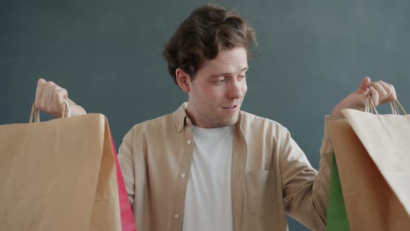 Slow Motion Portrait of Cheerful Young Man Holding Colorful Shopping Bags Smiling on Gray Background alt