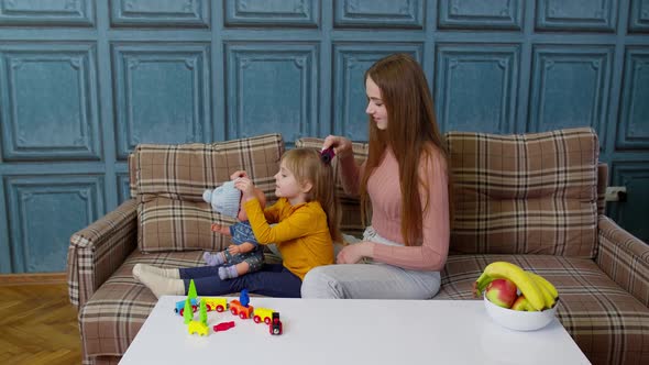 Mother Taking Care Brushing Hair of Daughter Child Girl in Living Room Kid Playing with Toy Doll alt