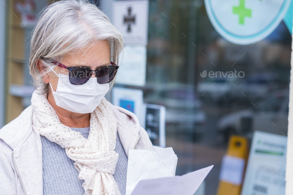 Covid-19. Senior lady wearing surgical mask and protective gloves leaves the pharmacy with medicines