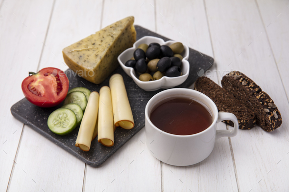 side view cup of tea with smoked cheeses with olives tomato cucumber and slices of black bread on a