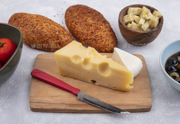 top view of yellow cheese with holes on a wooden kitchen board with knife with patties tomatoes and