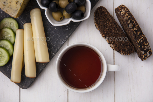 top view cup of tea with smoked cheeses with olives and slices of black bread on white background