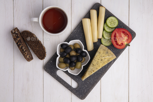 top view cup of tea with smoked cheeses with olives tomato cucumber and slices of black bread on