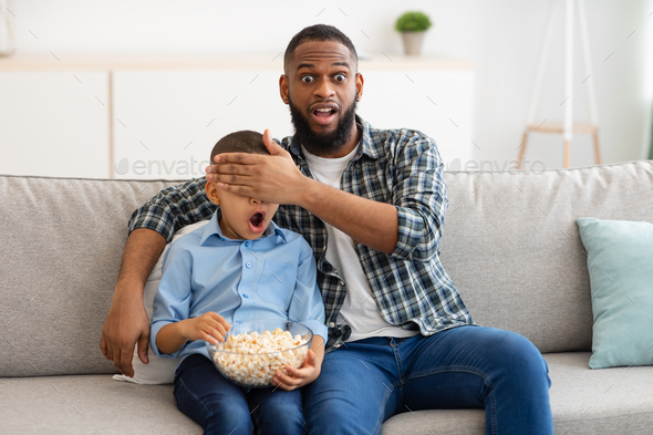 Shocked Father Covering Son\'s Eyes Watching Questionable TV Content Indoor