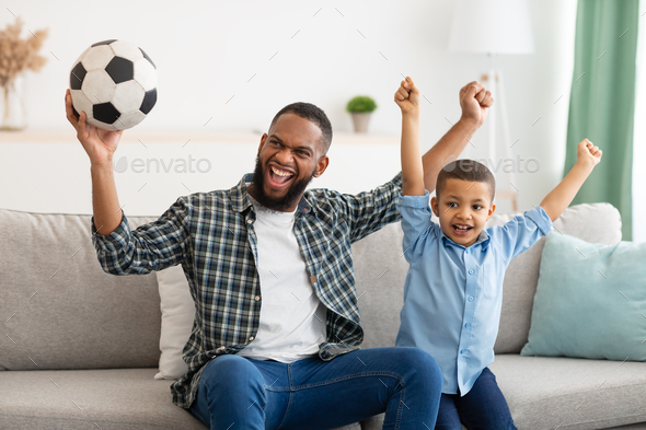 Joyful Daddy And Son Watching Soccer Game On TV Indoor