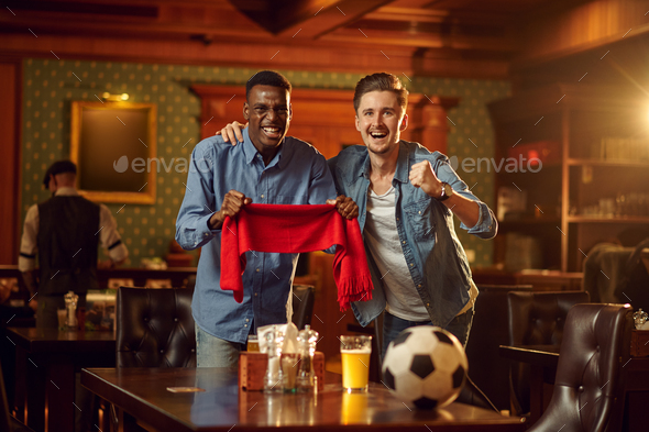 Two football fans with red scarf and ball in bar