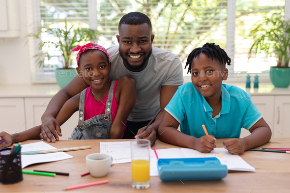 Portrait of african american father sitting at table helping son and ...