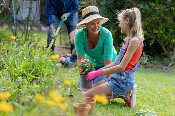 Smiling caucasian granddaughterl and grandmother talking in garden while gardening with their family