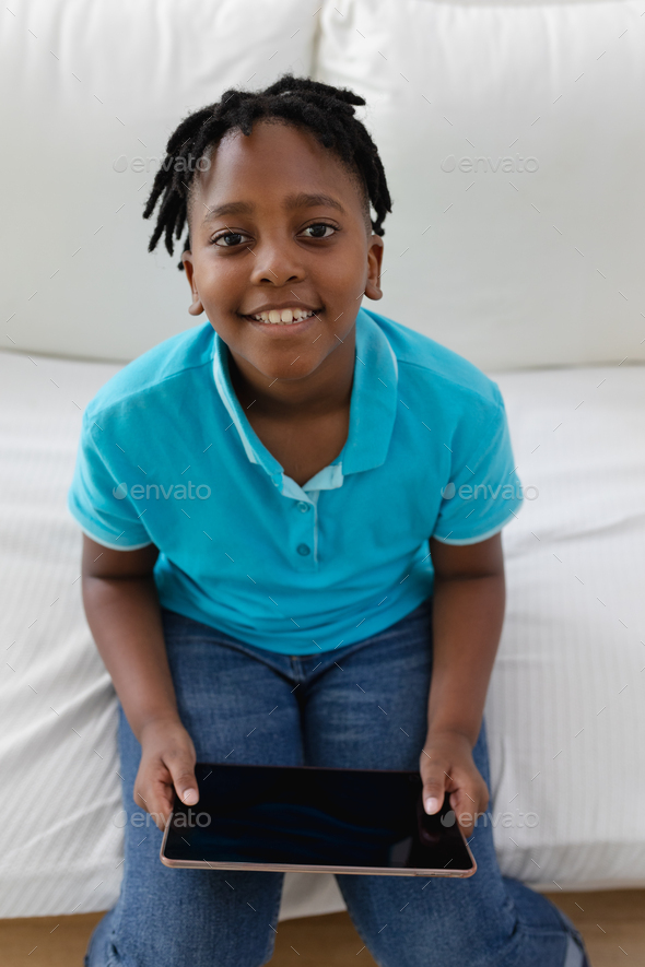 Portrait of smiling african american boy with short dreadlocks sitting on couch using digital tablet