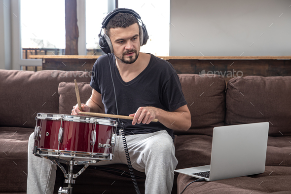 A young man with headphones learns to play the drum using online lessons.