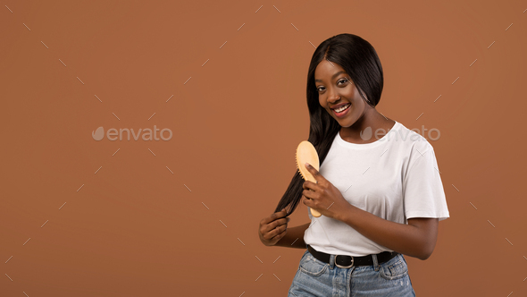 Happy black lady brushing her long hair with wooden brush