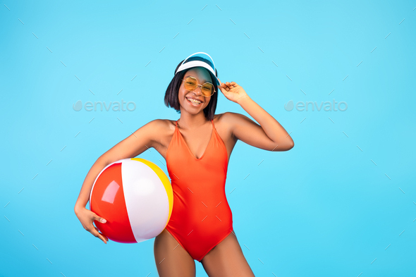 Carefree black woman in swimsuit posing with inflatable beach ball