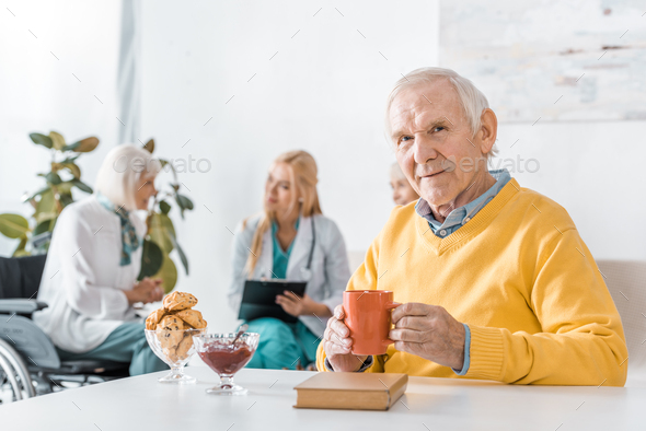 senior man drinking tea while doctor examining senior women