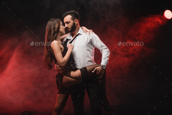 heterosexual passionate couple hugging in red smoky room