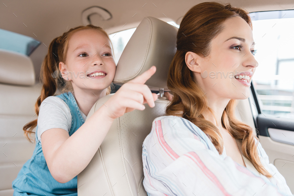 side view of smiling kid pointing away and mother driving car