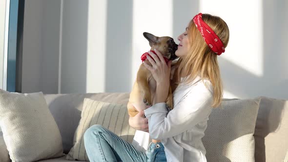 Young Woman in a White Shirt and Jeans Sits on the Sofa and Playing with Her Dog alt