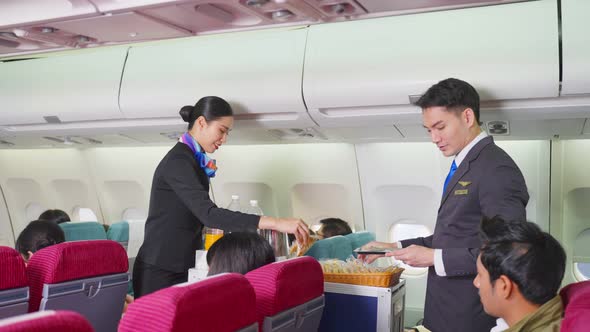 Asian male and female flight attendant walking on aisle to serve food and drinks to all passenger. alt