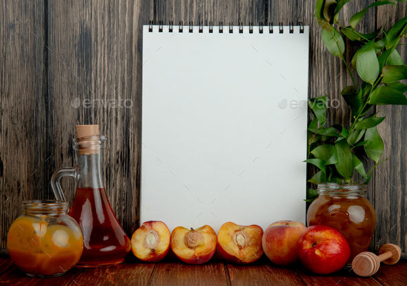 side view of cut and whole peaches with peach and plum jams with note pad on wooden background