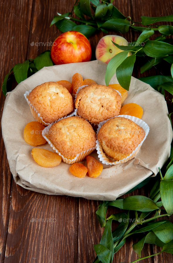 side view of cupcakes with dried plums in plate and peaches on wooden background decorated with