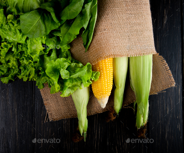 top view of cooked and uncooked corns in sack with lettuce and spinach on black background