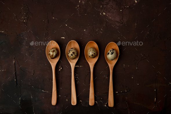 top view of wooden spoons with mini eggs on maroon background with copy space
