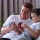 Father with Son Sitting on Sofa Indoors and Playing with Plastic Robots - VideoHive Item for Sale
