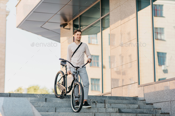 Confident young businessman walking with eco transport on street in town, going to work and active