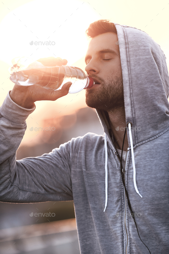 Staying hydrated. Confident young man drinking water while standing