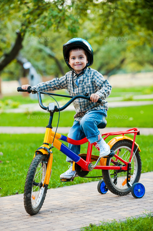 Little cyclist. Cheerful little boy looking at camera and smiling while ...