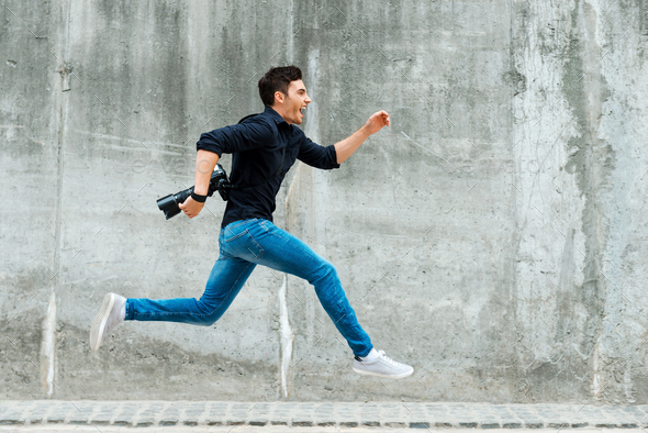 Hurrying to be first. Full length of young photographer running against a concrete wall