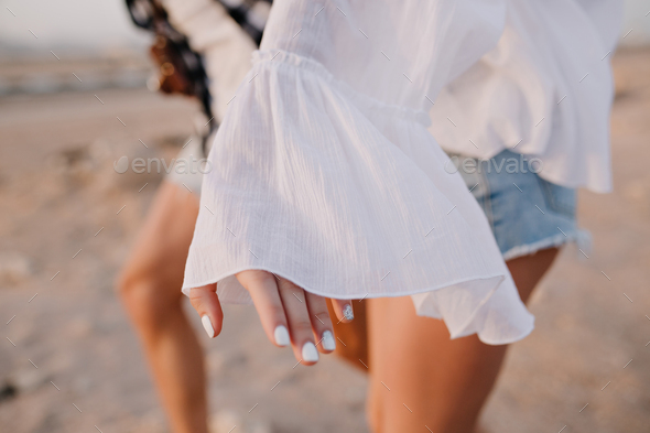 Graceful girl in vintage blouse and denim shorts with trendy white manicure having fun outside runni