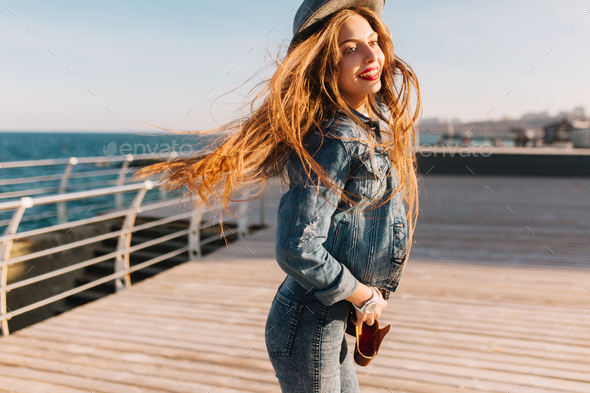 Cheerful brunette girl with everyday make-up jumping on the pier posing at sea background and smilin