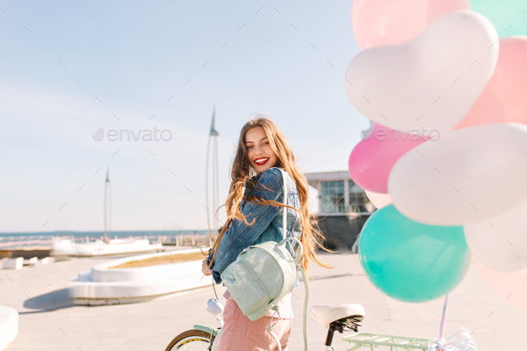 Smiling brunette girl came to the pier to let the colorful balloons into the blue sky. Portrait of g