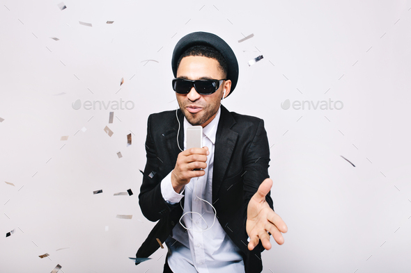 Happy party time of joyful handsome guy in hat, suit, black sunglasses having fun in tinsels on whit