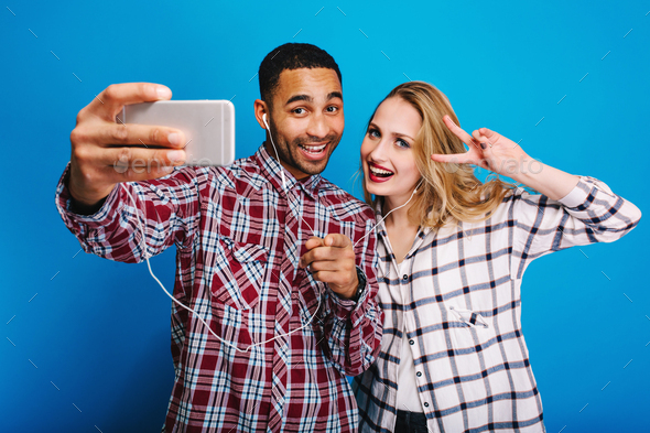 Stylish handsome guy making selfie portrait with attractive young woman with long blonde hair on blu