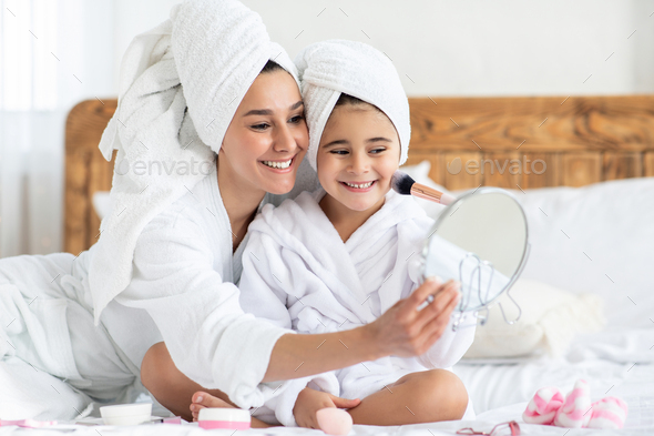 Mom tickling her cute little daughter with make up brush