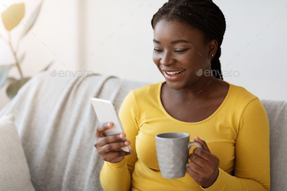 Pleasant Message. Happy Black Woman Using Smartphone And Drinking Coffee At Home - Stock Photo - Images