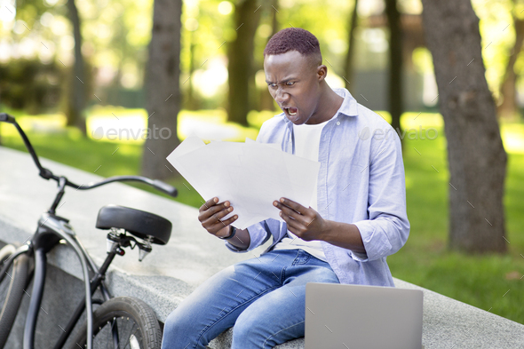 Online job. Young black freelancer with bike and laptop finding mistake in his work project