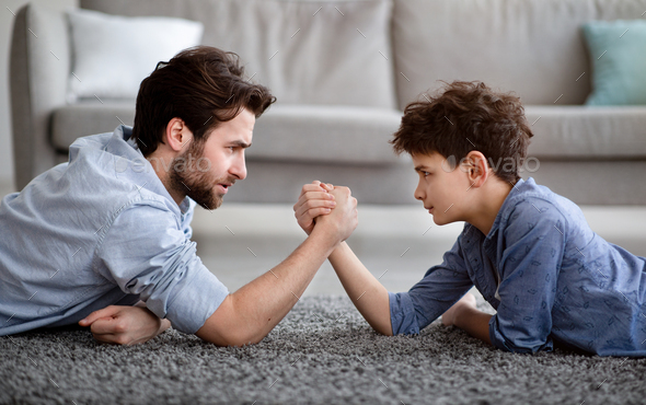Raising a real man. Concentrated father and son arm wrestling and competing while lying on floor - Stock Photo - Images
