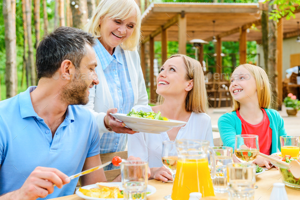 More Salad? Happy Family Enjoying Meal Together While Sitting At The ...