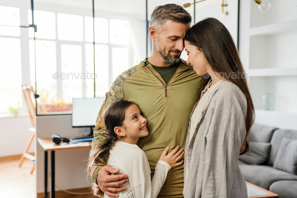 Happy masculine military man smiling and hugging his family indoors
