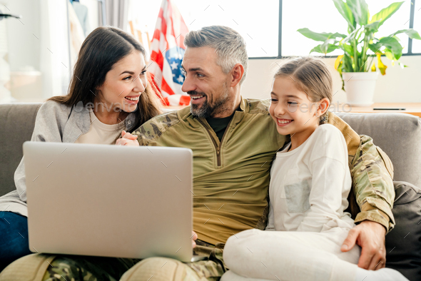 Happy military man smiling and hugging his family while using laptop