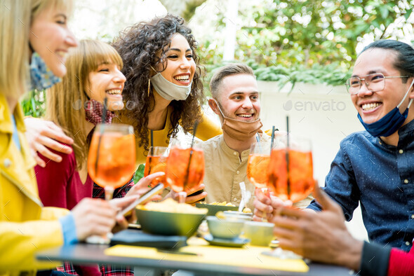 Multiracial friends wearing face masks drinking cocktails at bar restaurant