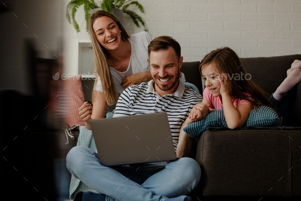 Young smiling family is watching funny videos on laptop computer. Happy  family time. Stock Photo by nebojsa_ki